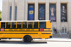 A school bus with children looking out is parked in front of the IU Auditorium.
